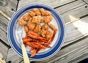 A plate of chicken nuggets and sweet potato fries on a wooden table.